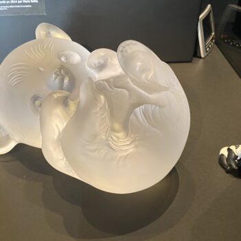 un grand bébé panda en cristal incolore sur le dos et à sa droite, deux petits pandas en plastique qui sont des jouets (1 panda adulte assis et un bébé panda)